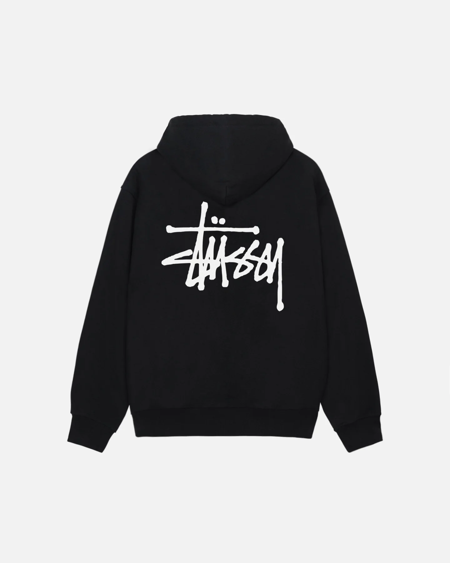 Un modèle portant un pullover Stüssy gris avec le logo emblématique, associé à un jean décontracté et des baskets blanches, pour un look urbain et moderne.